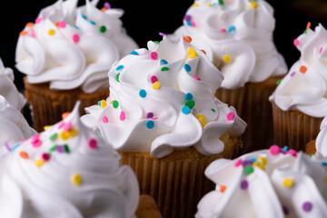 Fluffy vanilla cupcakes, with meringue and dragees on a black background.
