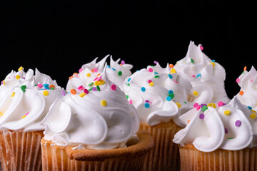 Fluffy vanilla cupcakes, with meringue and dragees on a black background.