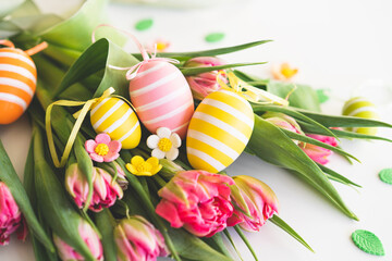 Happy Easter. Stylish dyed easter eggs with spring flowers on white background. Pink tulips with colorful eggs