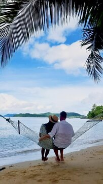 a mature couple relaxing in a hammock on the beach under a palm tree at the island of Koh Mak Trat Thailand