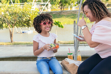 Woman and her daughter eating vegetables outdoors.