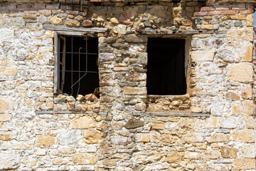 The window of an old stone house with a broken window in the foreground, ruins of an old house in the village. 