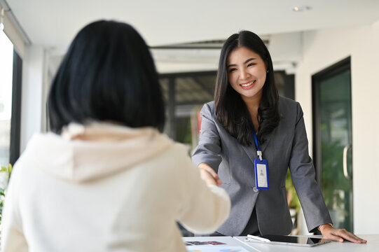 Attractive Asian businesswoman shaking hand with her business client in the office.