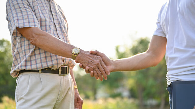 Cropped image of a businessman or supplier shaking hands with an elderly farmer