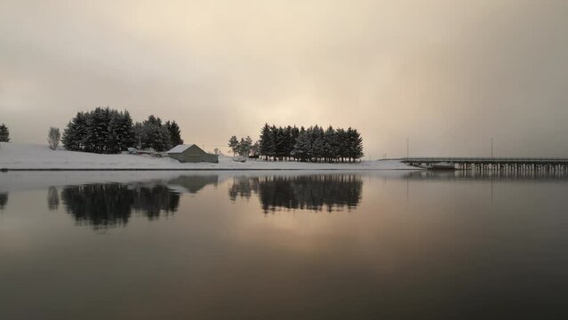 Drone flying low over smooth fjord waters surface on winter day, Kvaloya in Norway. Aerial sideways and space for copy