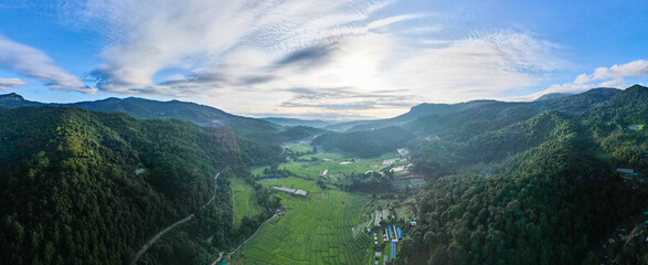 Panoramic view of rice fields and green mountains outdoors with clouds banging sun rays.