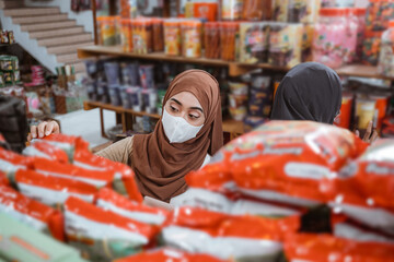 Muslim girl in mask choosing items while shopping in store - obrazy, fototapety, plakaty