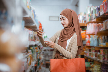 Muslim woman holding a drink bottle carrying a red bag in a supermarket
