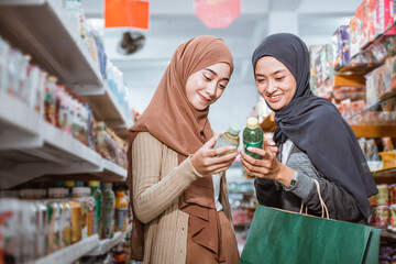 Two Muslim girls in masks observing items while shopping together in a store