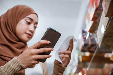 Muslim woman hands using cellphone and checking shopping receipt in supermarket