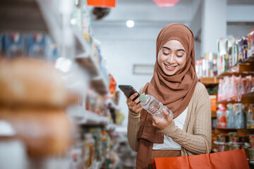 Muslim girl holding a mobile phone and a drink bottle while shopping in a store