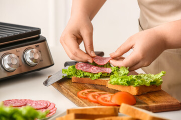 Woman preparing delicious sandwiches near modern electric grill in kitchen