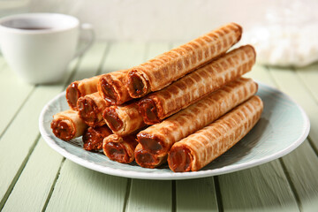 Plate of delicious wafer rolls with boiled condensed milk on green wooden table