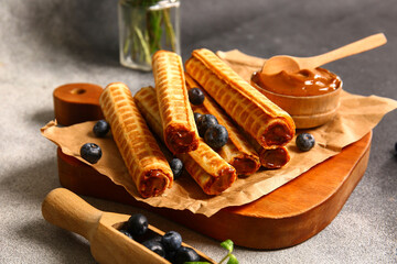Board of wafer rolls with boiled condensed milk and blueberries on grey grunge background