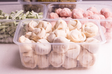 Frozen vegetables and semi-finished meat products in plastic containers on a white plate. meatballs, dumplings, chopped beans