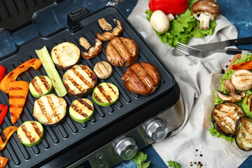 Modern electric grill with tasty vegetables on blue background