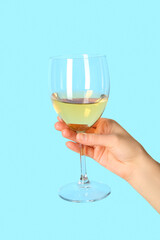 Female hand holding glass of white wine on blue background