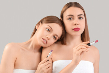 Young women with lipsticks on grey background, closeup