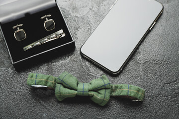 Male bow tie, mobile phone and cufflinks on dark background, closeup