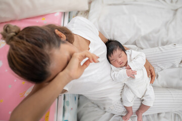 tired mother suffering from experiencing postnatal depression sitting on bed near children's cot....