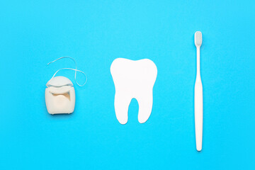 Dental floss, model of tooth and brush on blue background