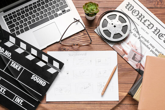 Storyboard with movie clapper, laptop and film reel on wooden background