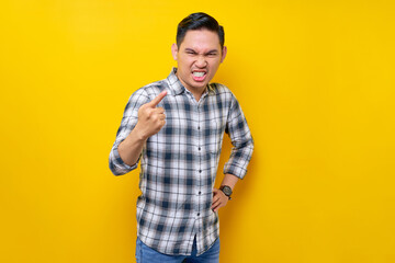 Young serious strict angry  Asian man in plaid shirt pointing finger at camera on you command do it isolated on yellow background. people lifestyle concept