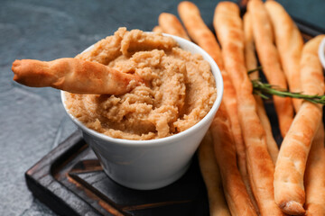 Wooden board with tasty Italian Grissini and hummus on dark background, closeup