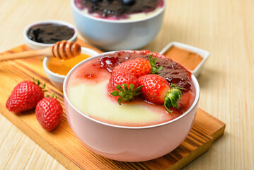 Bowl of tasty semolina porridge with strawberry jam, cinnamon and honey on light wooden table