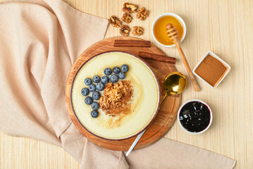 Bowl of tasty semolina porridge with blueberry, honey, cinnamon, jam and nuts on light wooden background