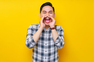 Portrait of excited young Asian man in plaid shirt screaming hot news about sales discounts with...
