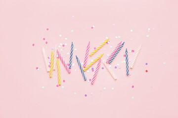 Colorful birthday candles and glitter on pink background