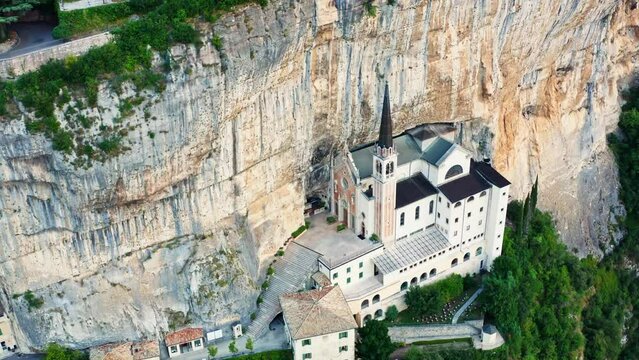 The aerial view of Madonna della Corona , Italy , during the morning golden hour displays the stunning mountaintop church perched precariously on a cliff, with the warm light.
