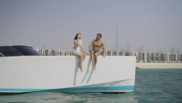Slow motion rotating shot of a young couple sitting on the edge of a yacht in Dubai