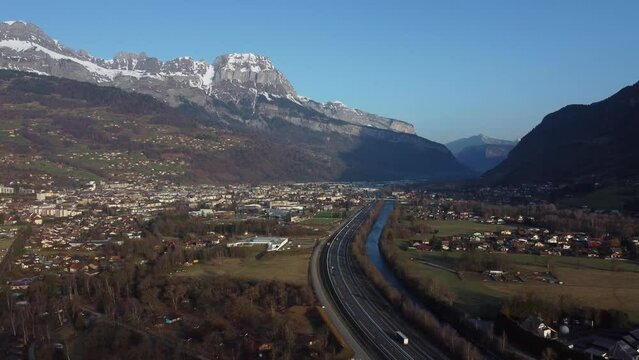 Aerial shot flying backwards over the Arve valley. Town of Sallanches in the background. Arve river and A40 highway, also called "Autoroute Blanche"