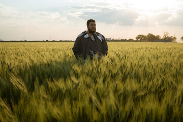 Naklejka na ściany i meble portrait of adult man standing in a wheat field at sunset