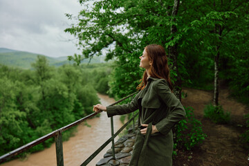 Naklejka na ściany i meble happy woman in a raincoat walks in the spring in the park near a stormy, mountain river
