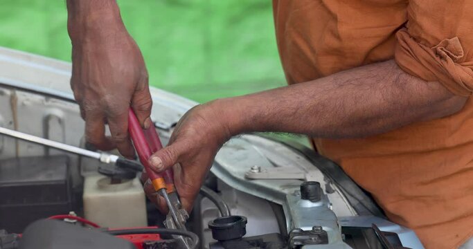 A man is fixing a car with pliers, or flat-nosed pliers, or wire cutters.