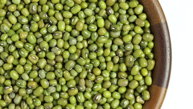 mung bean in wooden bowl rotating on white background, top view.