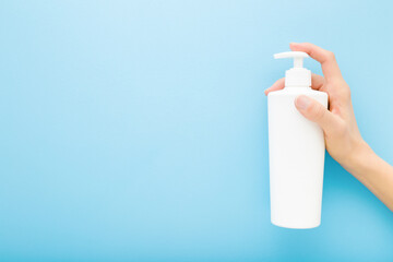 Young woman hand holding white big plastic pump bottle on light blue wall background. Pastel color....