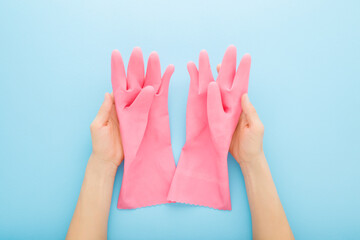 Young adult woman hands holding and showing new pink rubber protective gloves on light blue table background. Closeup. Point of view shot. Top down view.