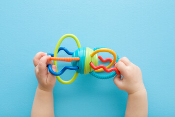 Baby boy hands playing with colorful rattle on light blue table background. Pastel color. Closeup....