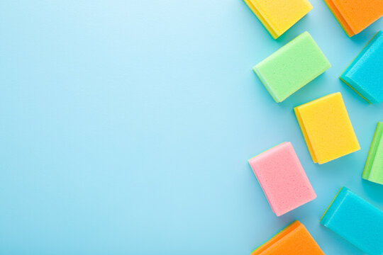 Row of new colorful dry sponges on light blue table background. Pastel color. Closeup. Cleaning products. Empty place for text. Top down view.