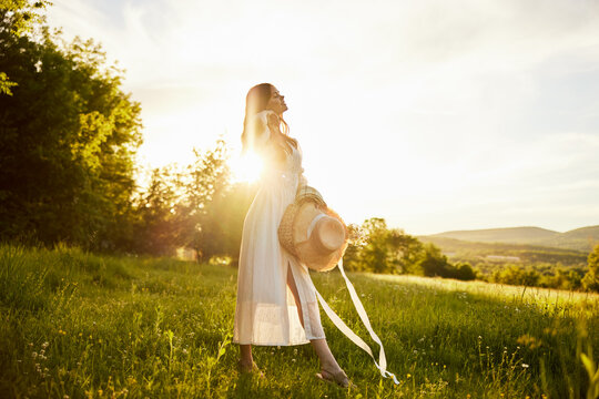 horizontal photo of a woman in a long light dress walking through the forest, illuminated from the back by the rays of the setting sun