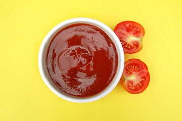 Tomato ketchup in a bowl on yellow background top view 