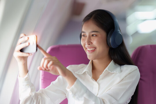 Beautiful Asian business woman taking a photo by mobile phone during flight in aeroplane. working, travel, business concept