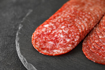 Sausage smoked salami cut into slices, on slate stone plate round, dark background, selective focus