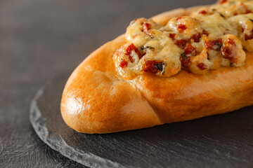 Pizza on baguette bread with salami and melted cheese, on slate stone plate round, dark background, selective focus