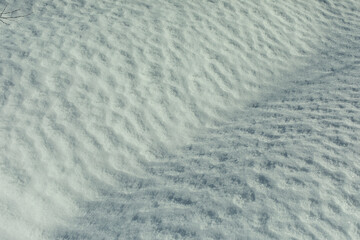 Texture of snow. Snow melts in spring. Waves on surface. Natural background is winter.