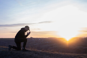 Prayer. Man on his knees praying. Against the background of the sky and sunset. Forgiveness of sins and repentance. Easter